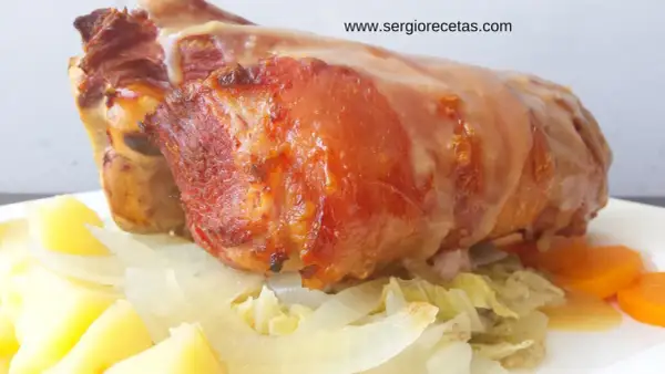 Codillo de cerdo asado, jugoso y dorado, servido con patatas, cebolla y zanahorias. ¡Un manjar!