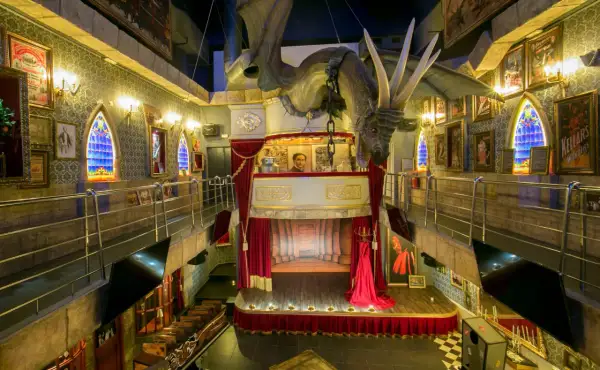 Dragón suspendido sobre un escenario teatral en el magic museum Peñíscola. Ventanas góticas y pósters de ilusionismo adornan las paredes.