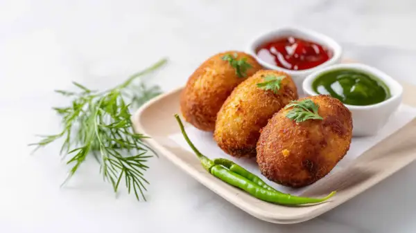 Croquetas de puchero doradas y crujientes, servidas con kétchup, salsa verde y guindillas.