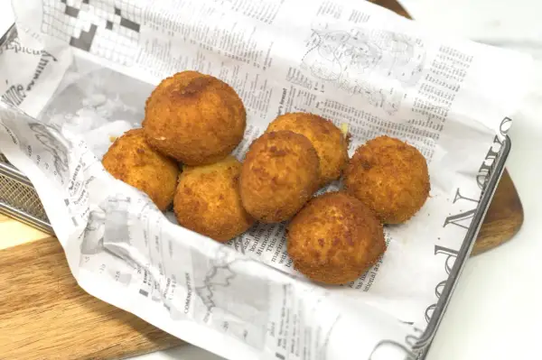 Croquetas de gambas doradas y crujientes, servidas en una bandeja con papel de periódico.