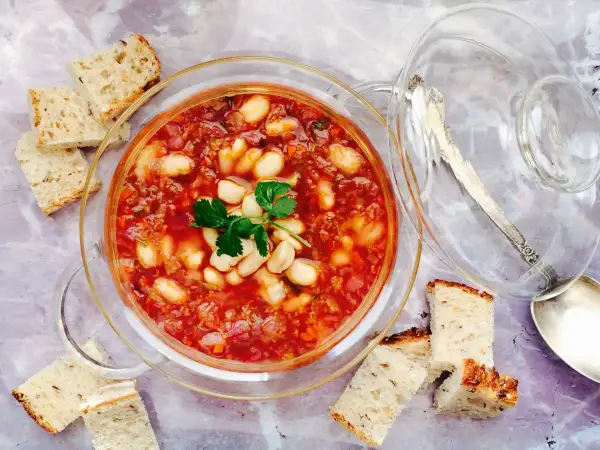 Un tazón de alubias con verduras, servido con pan rústico.