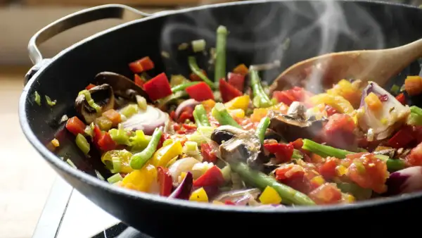 Un delicioso salteado de verduras humeante en un wok, con pimientos, judías verdes, champiñones y cebolla morada.