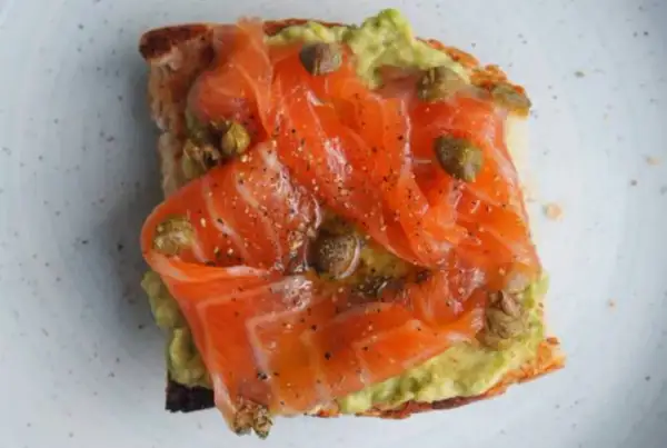 Tostada con aguacate y generosas lonchas de salmón marinado, aderezada con alcaparras y pimienta negra.