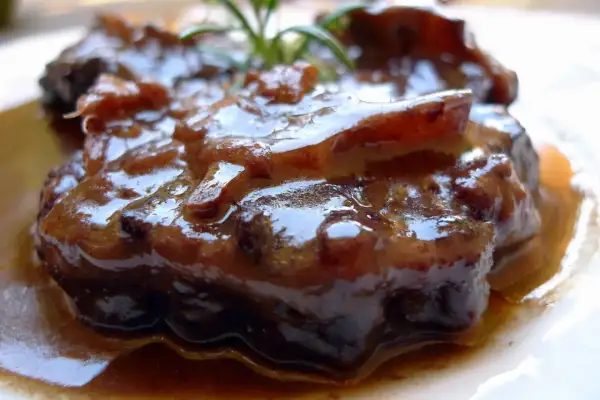 Un plato de rabo de toro estofado, jugoso y cubierto de una rica salsa oscura. Una ramita de romero decora la carne.