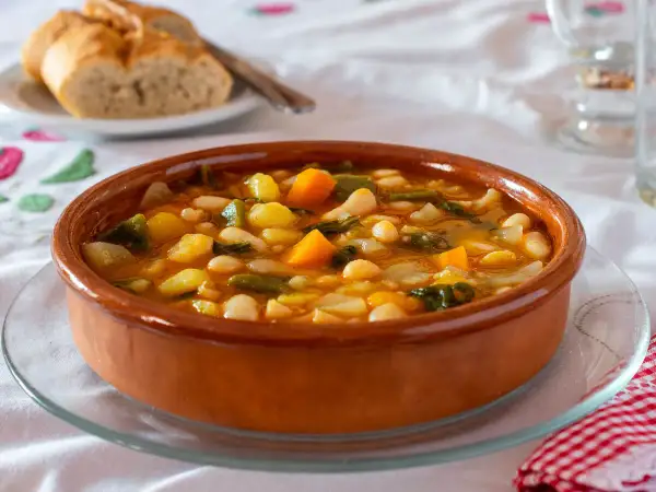 Un plato de barro con una sabrosa comida típica de Castellón: judías blancas, patatas, zanahoria y verduras en un caldo reconfortante.
