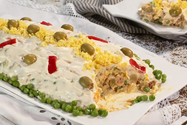 Ensaladilla rusa, receta de la abuela, cubierta de mayonesa, aceitunas, huevo rallado y pimientos.