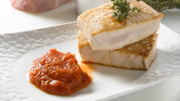 Dos trozos de atún a la plancha apilados, con una guarnición de salsa de tomate y una ramita de tomillo.