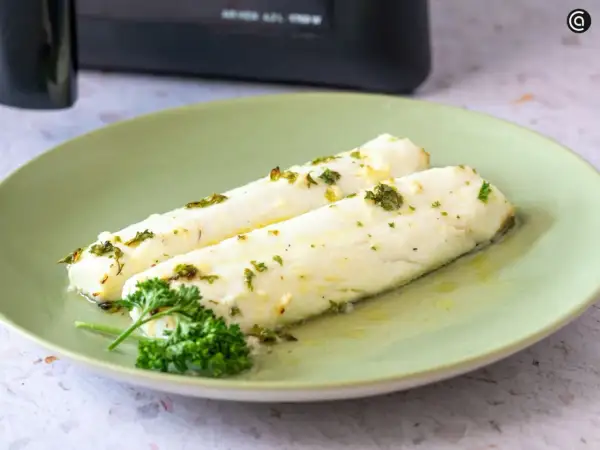Dos filetes de merluza jugosa, recién hechos en airfryer, con hierbas frescas y aceite de oliva.