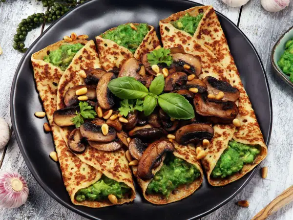 Crepes salados rellenos de aguacate y champiñones salteados, decorados con piñones y albahaca fresca.