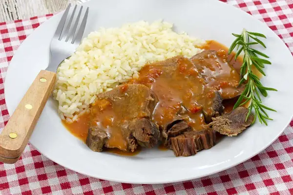 Deliciosa lengua en salsa con arroz blanco y una ramita de romero. Un plato reconfortante listo para disfrutar.