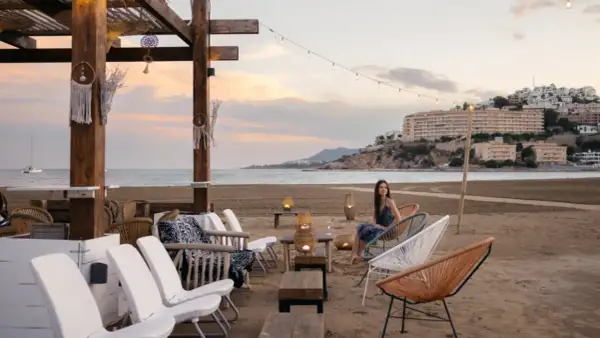 Una mujer disfruta de la tarde en la playa sur Peñíscola, sentada en una silla de diseño frente al mar.
