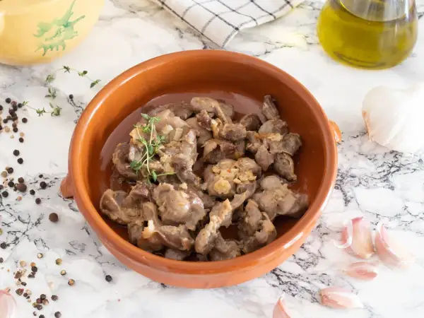 Mollejas de pollo guisadas con ajo y tomillo en cazuela de barro, acompañadas de granos de pimienta y una cabeza de ajo.