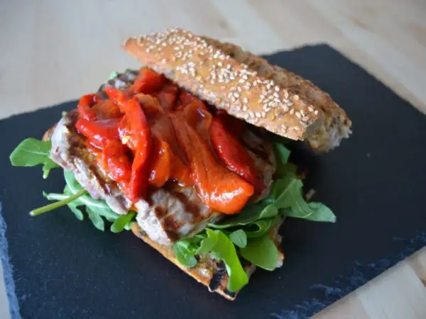 Un delicioso pepito de ternera con pimientos rojos asados y rúcula, servido en pan rústico con semillas.