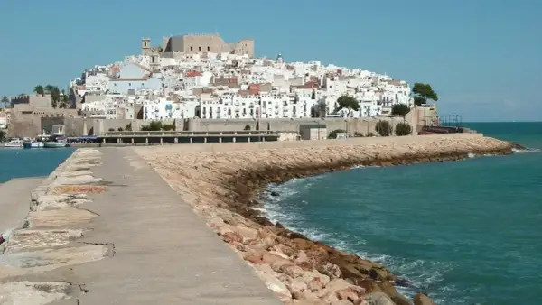 Pueblos costa Azahar: un castillo y casas blancas se alzan sobre una colina, con el mar turquesa y un rompeolas de rocas.