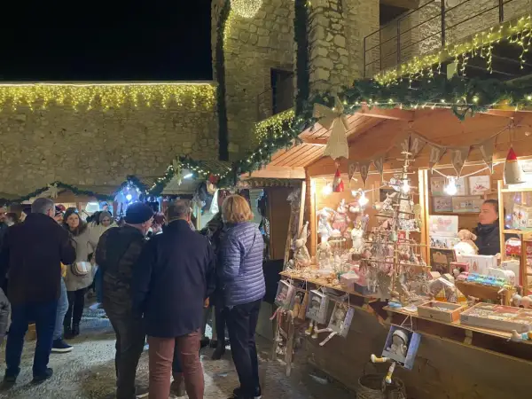 Gente pasea por el mercado navideño Peñíscola, con puestos de adornos y luces festivas.