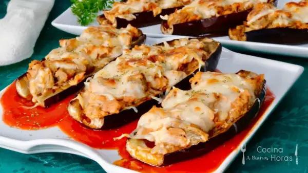 Berenjenas rellenas de atún gratinadas con queso, servidas sobre una base de salsa roja.