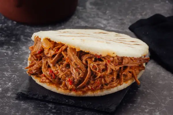 Arepa rellena de carne mechada jugosa y tierna, con trozos de pimiento rojo.