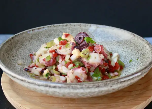 Salpicon de pulpo fresco con pimientos, cebolla y perejil, servido en un cuenco rústico.