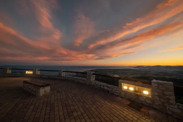 Atardecer espectacular sobre el mar y la costa. Un mirador perfecto para ver qué ver en Alcossebre, con un banco y luces que invitan a contemplar.
