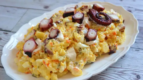 Deliciosa ensaladilla de pulpo con patatas, huevo y zanahoria, coronada con trozos de pulpo tierno y un toque de mayonesa.