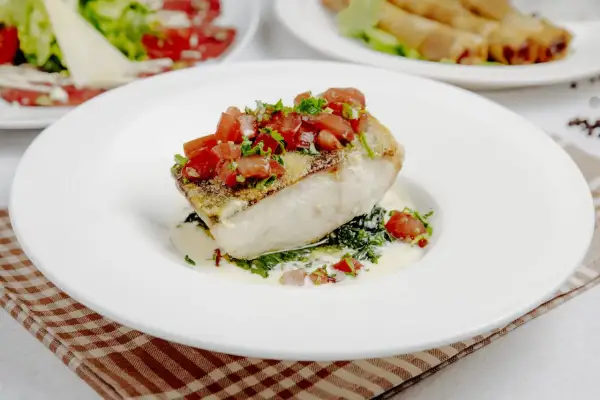 Filete de bacalao con tomate y hierbas, sobre espinacas y salsa cremosa. Un plato principal ideal para tus recetas de bacalao.