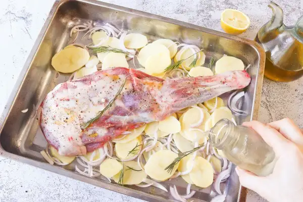 Paletilla de cordero al horno lista para asar con patatas, cebolla y romero. Un chorrito de aceite y al horno.