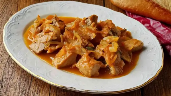 Sabroso atún encebollado en una salsa dorada, servido en un plato blanco con borde dorado.