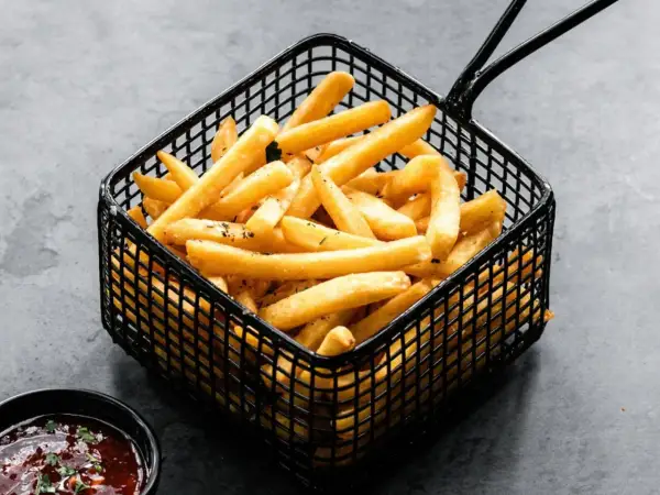 Patatas soufflé doradas y crujientes en una cesta negra, listas para ser disfrutadas con una salsa.