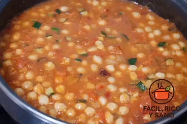 Un guiso casero de garbanzos con verduras, como calabacín y tomate, burbujeando en una olla.