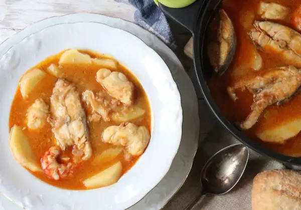 Un plato humeante de suquet de pescado, con trozos de pescado blanco, patatas y gambas en una rica salsa.