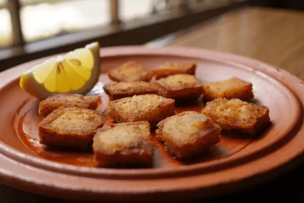 Deliciosos trozos de bacalao rebozado, dorados y crujientes, servidos en un plato de barro con una rodaja de limón.