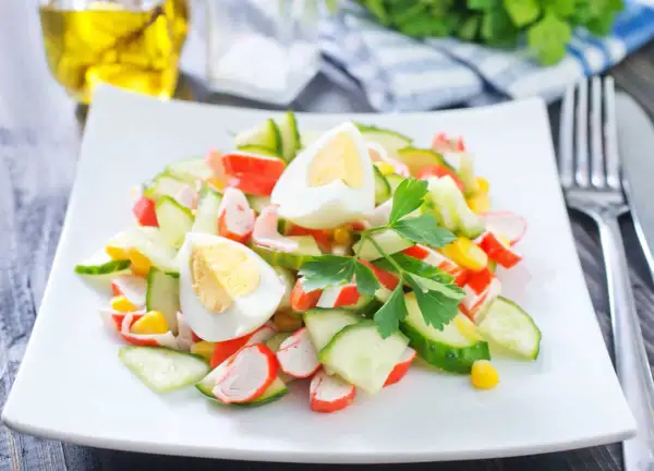Deliciosa ensalada de cangrejo con pepino, huevo cocido y maíz, decorada con perejil fresco.