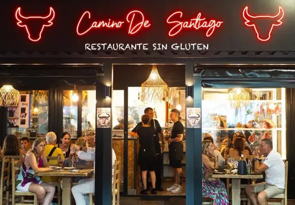 Restaurante "Camino de Santiago" en Peñíscola, con letrero de neón y comensales disfrutando de una comida.