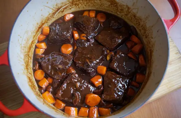 Boeuf bourguignon cocinado a fuego lento en una olla roja, con trozos de carne tierna, zanahorias y champiñones en una rica salsa.